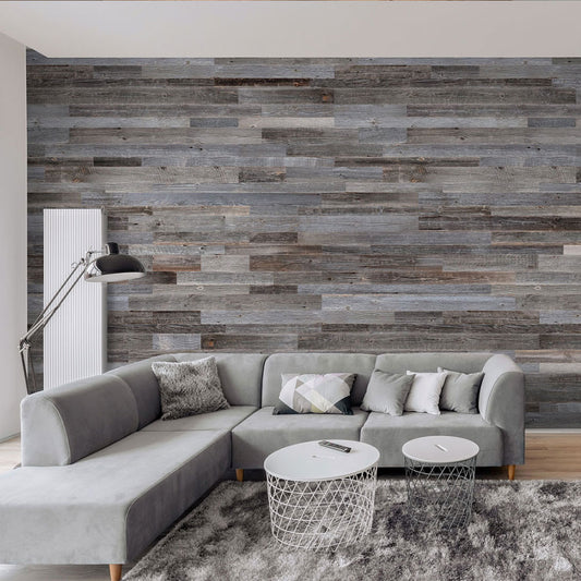 Un salon moderne comprenant un canapé sectionnel gris, des coussins géométriques, des tables basses rondes blanches, un tapis gris, un lampadaire noir et un mur d'accent Wood & Wall Decor™ Parement Bois Anthracite avec des nuances de gris et de marron.