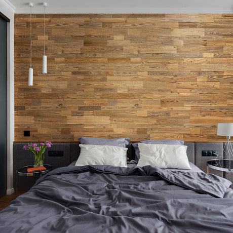 Une chambre à coucher moderne dotée d'un mur d'accent en bois Parement Bois Grange Lite de Wood & Wall Decor™, de lampes suspendues, d'un lit double avec une literie grise et des oreillers blancs, ainsi que de tables d'appoint avec des fleurs violettes et une lampe, crée une retraite sereine.
