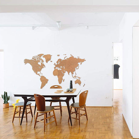 Une salle à manger moderne comprend une table en bois foncé, quatre chaises marron dans une disposition flexbox, un petit cactus en pot, et l'art mural World Map™ Carte du monde en Bois 280x170cm - Marron - Géante sur un mur blanc. Le parquet mène à une porte ouverte.