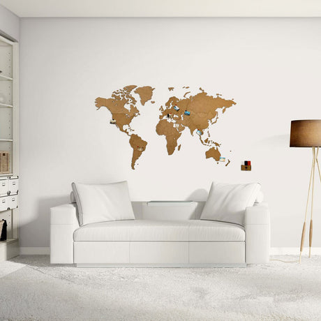 Un salon moderne présente la World Map™ "Carte du monde en Bois 130x78cm - Marron" au mur, avec des épingles marquant les destinations, un canapé blanc et une décoration minimaliste - ce qui en fait un lieu idéal pour les amateurs de voyage en quête de style et d'inspiration.