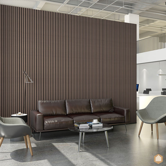 Salon de bureau moderne avec un canapé en cuir brun, une table basse en verre, des fauteuils gris et un mur d'accent Panneau Tasseau Acoustique en Chêne fumé 3 Faces by Acoupanel™. Un bureau de réception et un plafond ouvert sont visibles à l'arrière-plan.