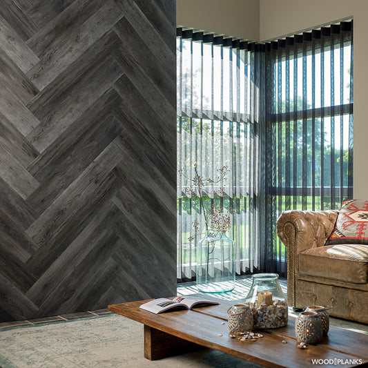 Un salon confortable avec un canapé en cuir marron, une table basse en bois et un vase en verre. De grandes fenêtres avec des stores verticaux éclairent l'espace. Un mur est décoré de Wood Look Planks™ Lambris PVC mural bois - chêne gris anthracite pour une touche de modernité.
