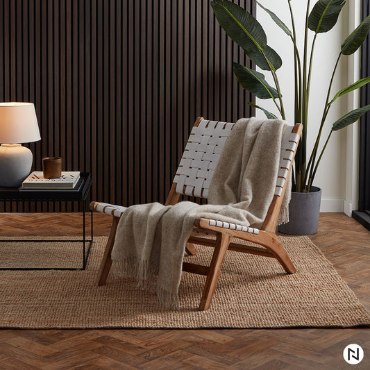 Un salon moderne comprenant une chaise longue en bois tressé avec un jeté beige, un tapis en jute et des panneaux muraux NatureWall™ Panneau Tasseaux Bois Acoustiques - Chêne fumé pour un style homogène et harmonieux.