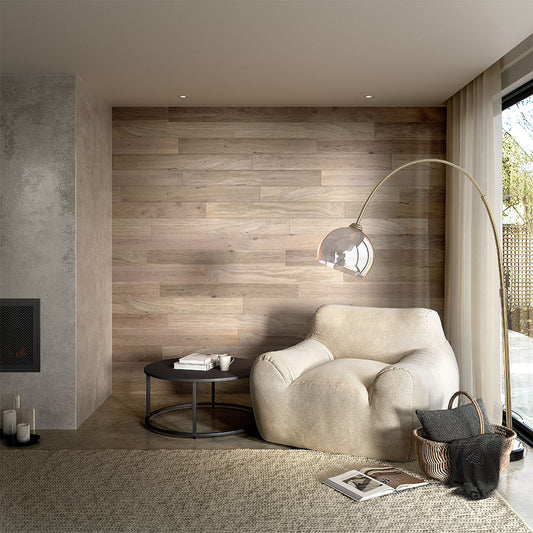 Un coin salon confortable comprend un fauteuil beige cossu, une table basse noire, un panier tressé et un lampadaire en arc - parfait pour se détendre à côté d'une grande fenêtre et du mur lambrissé revêtu de NatureWall™ Lambris Bois Adhésif Bois Flotté.