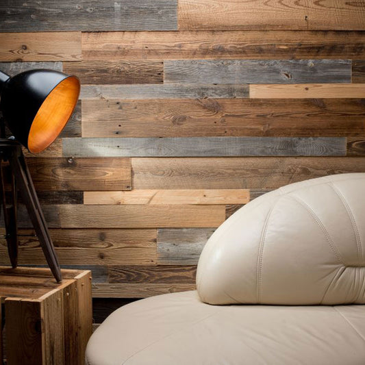 Un intérieur moderne avec une chaise en cuir fauve, un lampadaire trépied noir et un mur Wood & Wall Decor™ Parement Bois Antik à panneaux de bois pour une atmosphère rustique et chaleureuse.