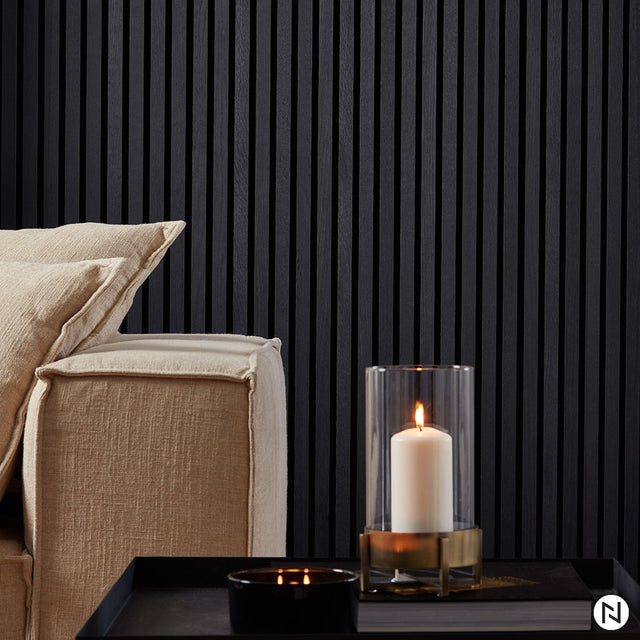 Un canapé beige confortable avec des coussins texturés se trouve à côté d'une table noire surmontée d'une bougie blanche, le tout placé contre le Panneau Tasseaux Bois Acoustiques - Chêne noir de NatureWall™ pour une toile de fond épurée et moderne.