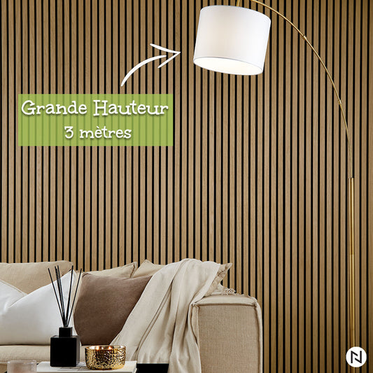 Un salon moderne présente un canapé beige, des coussins neutres et un lampadaire arqué de 3 mètres de haut par un mur à lattes NatureWall™ Panneau Tasseaux Bois Acoustiques - Chêne Naturel - Grande Hauteur. Une table accueille le décor. Texte : Grande Hauteur 3 mètres.