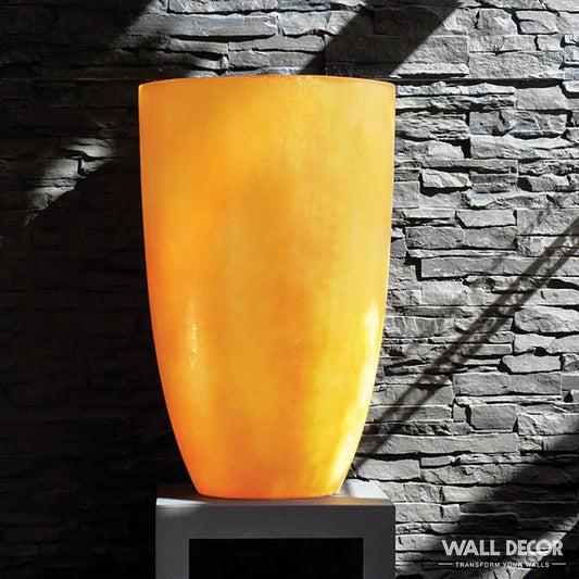 Un grand vase orange incandescent est posé sur un piédestal contre un mur texturé Plaque Pierre Noire ardoise - Laja (2,85m x 1,3m) par Covering Panels™, éclairé par la lumière du soleil. La mention "WALL DECOR" apparaît dans le coin inférieur droit.