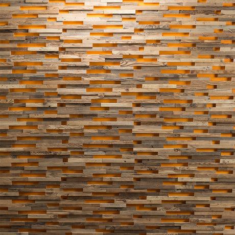 Parement Bois Visio by Wood & Wall Decor™ présente des planches de bois empilées de manière irrégulière avec des interstices, permettant à la lumière orange chaude de briller à travers et créant un aspect de mur texturé et stratifié.