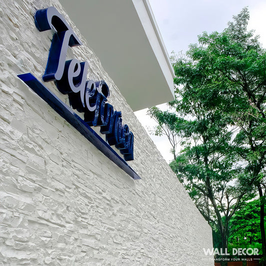 Un mur blanc texturé avec Plaque Pierre Blanche - Laja (2,85m x 1,3m) by Covering Panels™ présente un panneau Telejimen bleu foncé, en relief. Des arbres verts et un ciel nuageux apparaissent en arrière-plan.