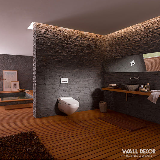 Salle de bains moderne avec murs en pierre sombre en Covering Panels™ Plaque Pierre Noire ardoise Laja (2,85m x 1,3m), toilettes flottantes, sol en bois, grand miroir au-dessus du lavabo, baignoire en arrière-plan et éclairage doux mettant en valeur le mur texturé.