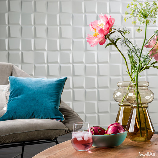 Un salon moderne avec une chaise grise, un coussin en velours sarcelle, une table en bois avec une boisson glacée et des pommes rouges, et un vase avec des fleurs roses devant le Panneau Mural 3D Oberon de WallArt Wall Decor© (boîte de 12 panneaux, 3m²) dans un style contemporain.
