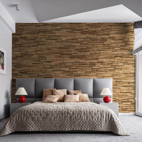 Une chambre à coucher moderne comprend un grand lit avec une tête de lit gris touffeté et une literie beige. Le mur du fond présente Wood & Wall Decor™ Parement Bois Taïga, tandis que des tables de chevet avec des lampes rouges ajoutent un style inspiré des mises en page CSS épurées.