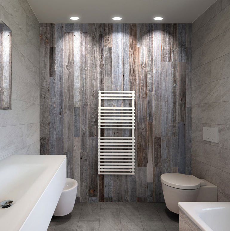 Salle de bain moderne comprenant un mur d'accent en bois Parement Bois Anthracite de Wood & Wall Decor™, un radiateur sèche-serviettes mural blanc, un lavabo flottant, un bidet, des toilettes ; des carreaux de sol gris et des luminaires encastrés au plafond complètent l'espace.