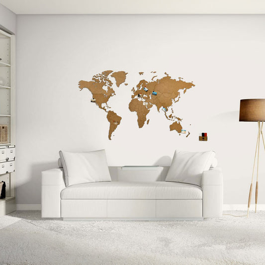 Un salon moderne présente la World Map™ "Carte du monde en Bois 130x78cm - Marron" au mur, avec des épingles marquant les destinations, un canapé blanc et une décoration minimaliste - ce qui en fait un lieu idéal pour les amateurs de voyage en quête de style et d'inspiration.