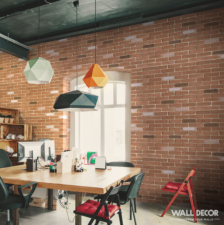 Bureau moderne présentant des murs Panespol™ Parement Brique Rouge - English Brick, une table en bois, des chaises dépareillées, des suspensions géométriques colorées et une grande fenêtre remplissant l'espace de travail de lumière naturelle. Logo WALL DECOR en bas à droite.