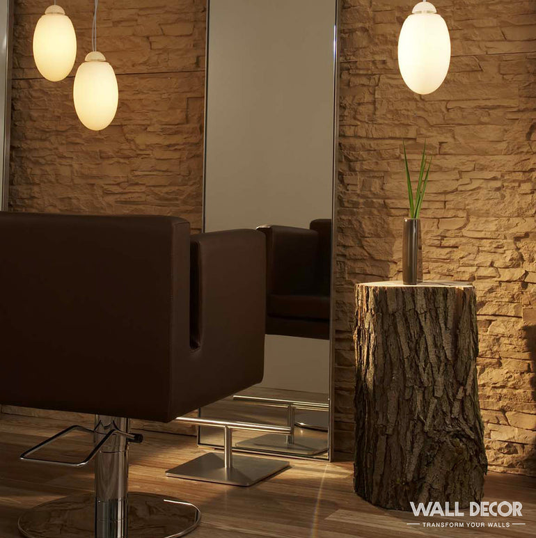 Un salon moderne comprend un fauteuil de coiffure marron face à un grand miroir, avec un mur Plaque Pierre Ocre - Laja by Covering Panels™, deux lampes suspendues ovales, et une table d'appoint rustique en forme de souche d'arbre avec un diffuseur en roseau. La marque apparaît dans l'angle.