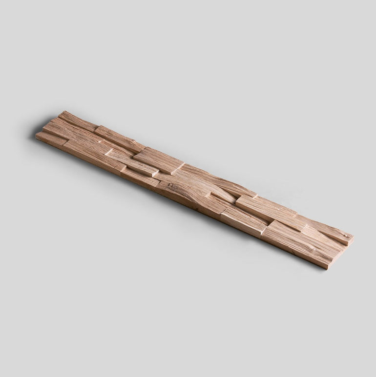 Un échantillon d'Échantillon Parement Bois by Wood & Wall Decor™ est présenté en diagonale sur un fond gris clair, présentant une pièce de bois longue et étroite avec une surface sculptée irrégulière et géométrique - choisissez le motif de votre choix !.