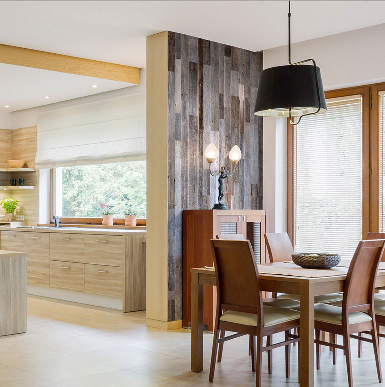Cuisine et salle à manger modernes présentant Wood & Wall Decor™ Parement Bois Anthracite sur le mur d'accent, avec des armoires en bois, une table en bois clair pour quatre personnes, une lampe suspendue noire et de grandes fenêtres laissant entrer la lumière naturelle.