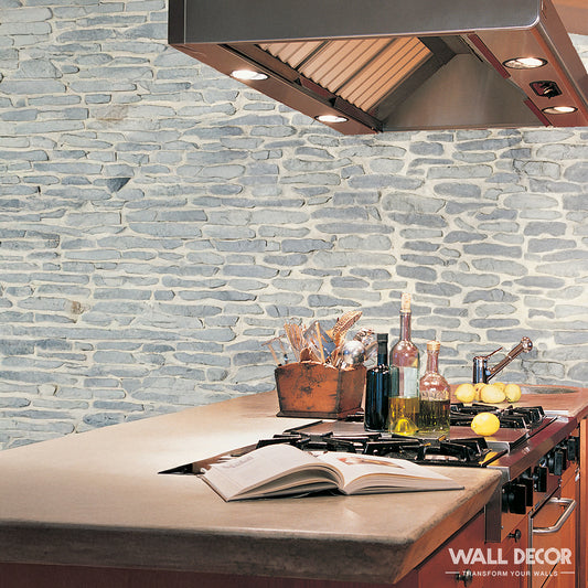 Une cuisine moderne présente un Covering Panels™ Plaque Pierre grise - Pierres gneiss Ascona (2,85m x 1,3m : 3,7 m²) mur d'accent, des appareils électroménagers en inox, des ustensiles et un livre de cuisine ouvert. Le logo "WALL DECOR" apparaît dans l'angle.