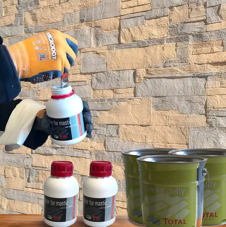 Une personne portant des gants ouvre une bouteille Covering Panels™ blanche du Kit de Finition Parement Mural, à côté de deux bouteilles assorties et de deux boîtes de Powder Putty vertes, le tout disposé contre un mur de pierre.