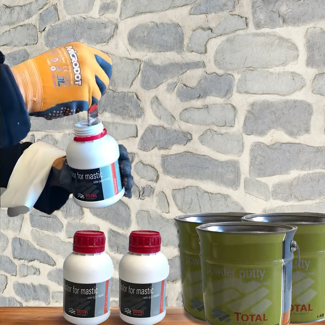 Portant des gants, quelqu'un ouvre un petit conteneur blanc Covering Panels™ "Kit de Finition Parement Mural : Kit Pour poser 12 Panneaux" devant un mur en pierre ; deux conteneurs similaires et des pots de peinture verts se trouvent à proximité.