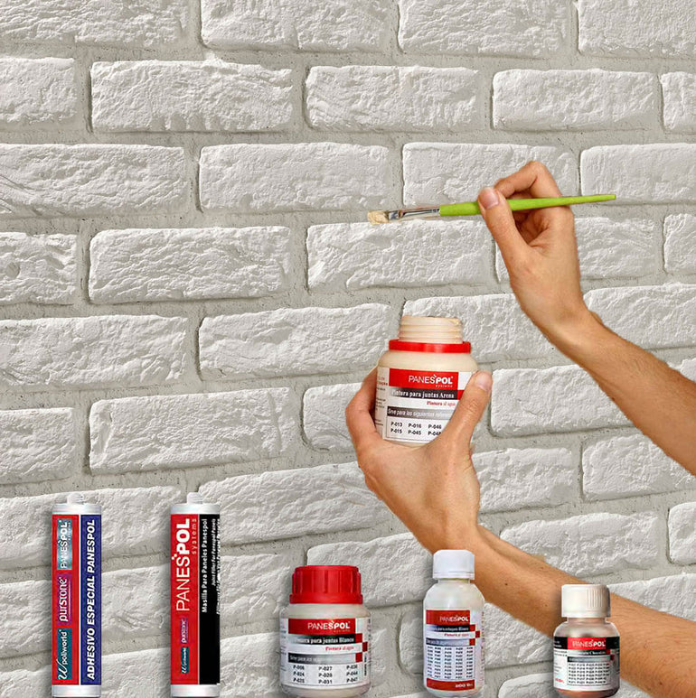 Une personne utilise un petit pinceau pour appliquer de l'adhésif Panespol™ Kit de Finition Parement Brique blanc sur un mur de briques blanches, avec divers récipients et tubes Panespol™ Kit de Finition disposés au fond.