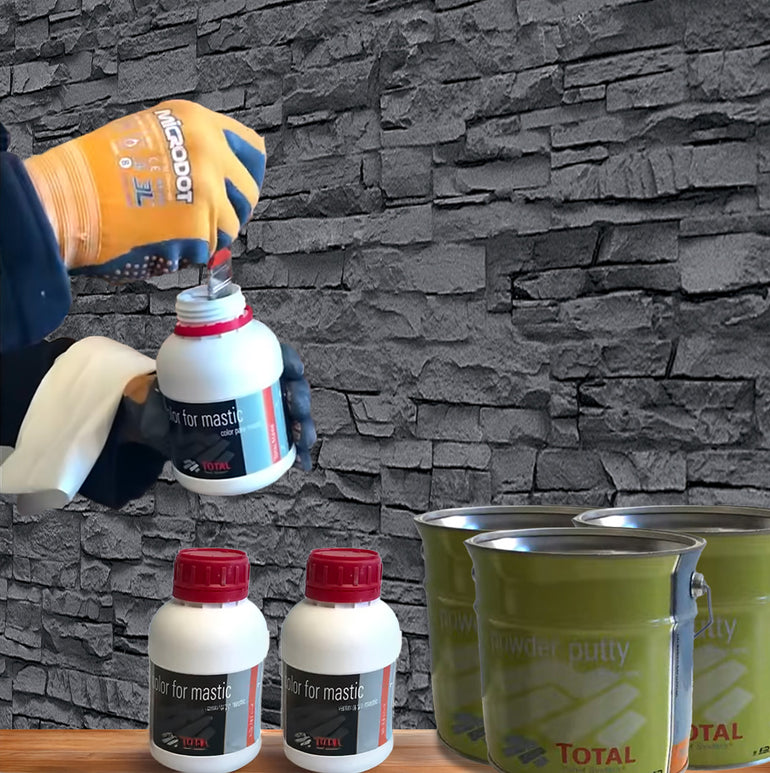 Une personne portant des gants ouvre un conteneur Kit de Finition Parement Mural blanc de Covering Panels™, avec deux conteneurs similaires et des bidons de mastic en poudre vert sur une surface en bois devant un mur en pierre grise.