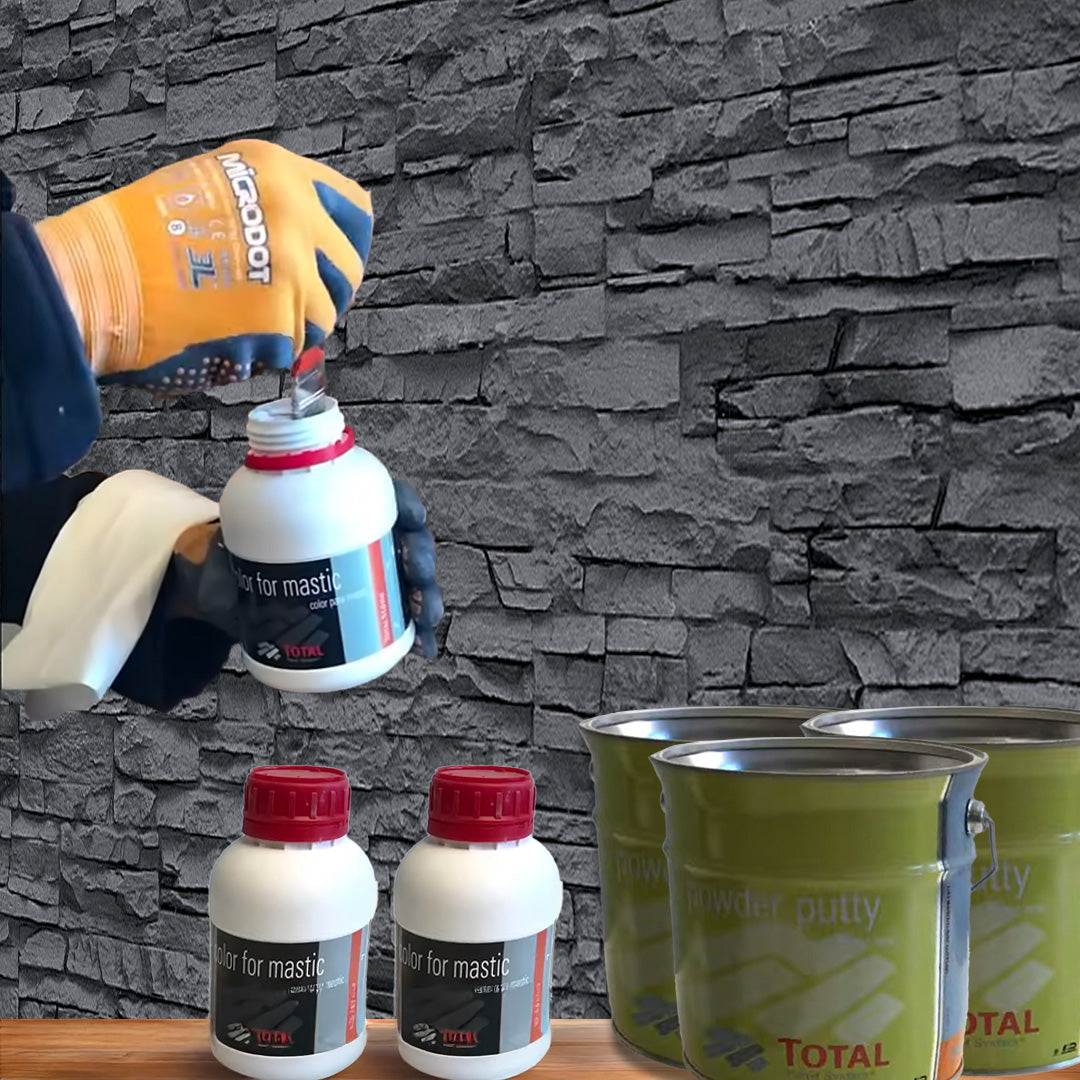 Une personne portant des gants ouvre un conteneur Kit de Finition Parement Mural blanc de Covering Panels™, avec deux conteneurs similaires et des bidons de mastic en poudre vert sur une surface en bois devant un mur en pierre grise.