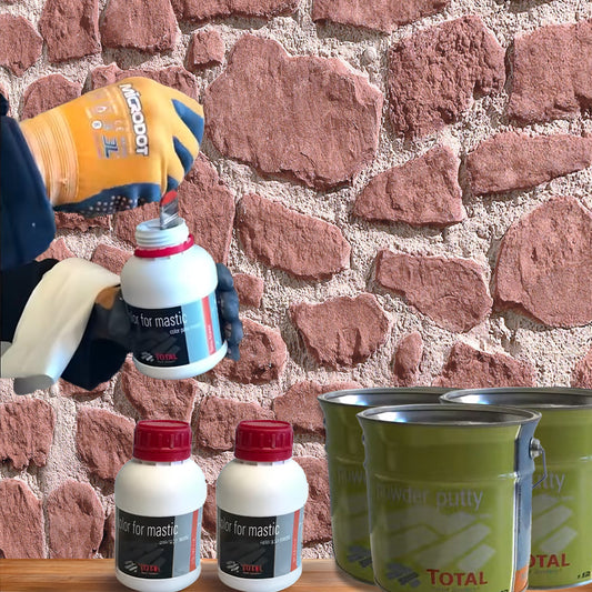 Une personne portant des gants de protection ouvre un petit récipient de Covering Panels™ Kit de Finition Parement Mural près d'un mur en pierre. Sur une table grise, il y a deux autres récipients identiques et trois bidons verts du kit.