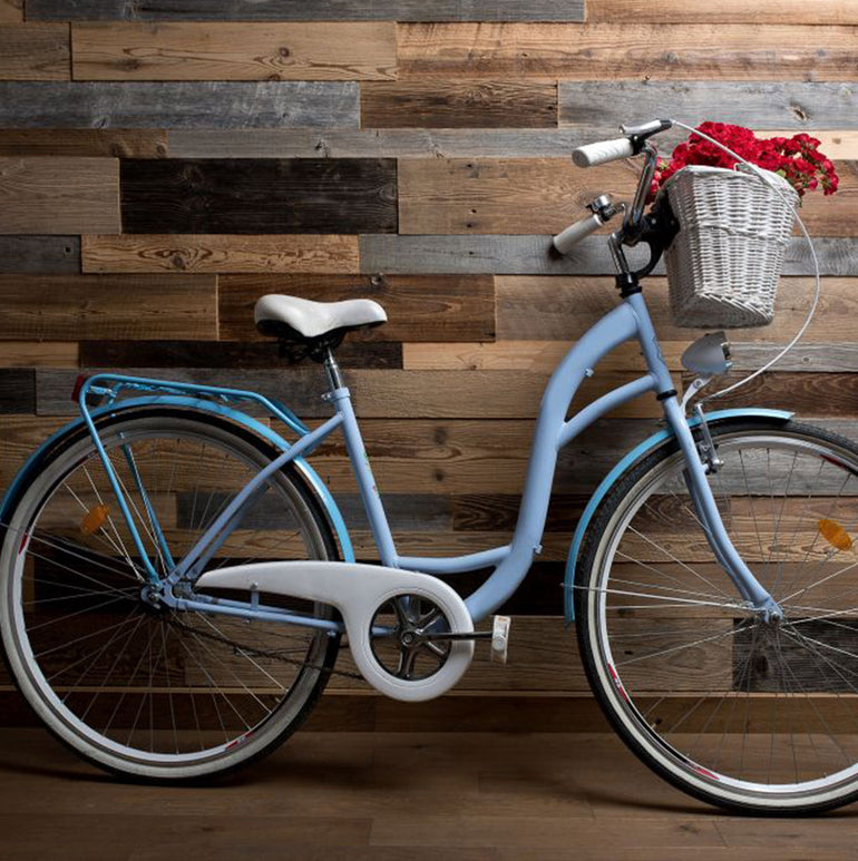 Un vélo bleu clair avec une selle et un guidon blancs se tient à l'intérieur contre un mur en planches de bois Parement Bois Antik par Wood & Wall Decor™, rehaussé par un panier en osier blanc contenant des fleurs rouges - idéal pour une description de produit qui attire l'attention.