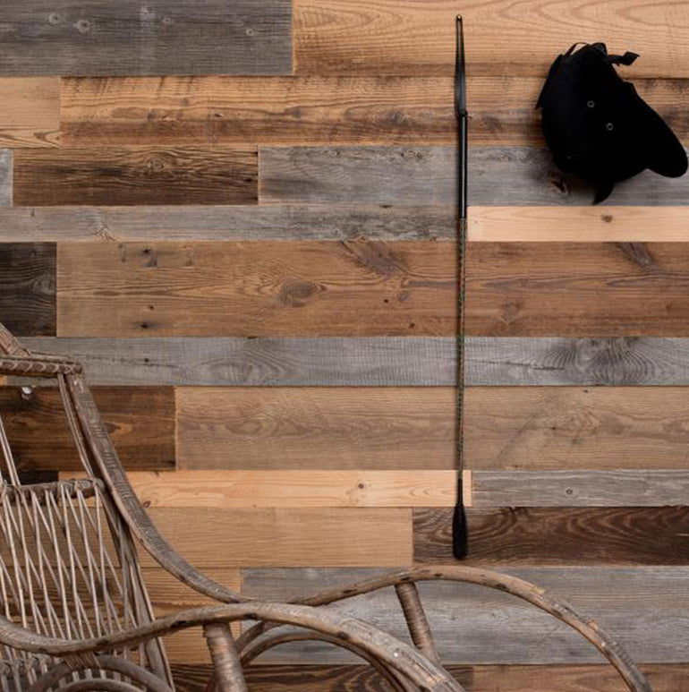 Parement Bois Antik by Wood & Wall Decor™ présente des planches de bois rustiques de couleur marron et grise, créant un mur d'accent chaleureux et vintage, parfait comme toile de fond pour un décor tel qu'une chaise en osier et des accessoires élégants.
