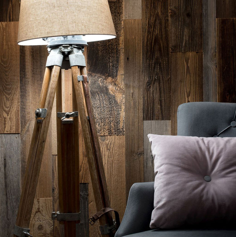 Un lampadaire tripode avec un abat-jour beige se trouve à côté d'un fauteuil gris avec un oreiller violet clair, placé contre Wood & Wall Decor™ Parement Bois Antik panneaux de bois rustiques-partagez la description de votre produit pour améliorer les détails.