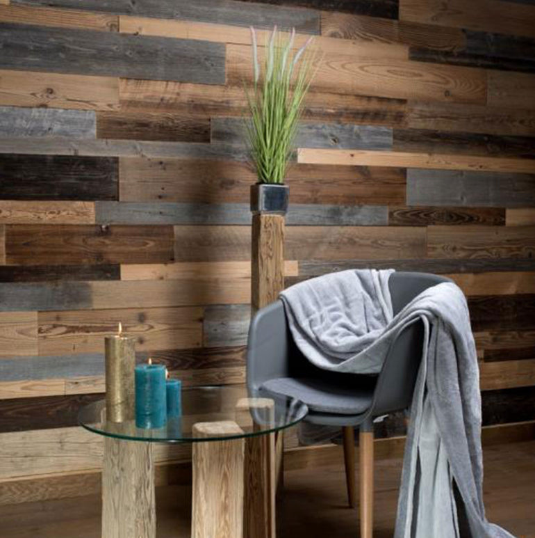 Une pièce moderne avec un mur d'accent en bois Parement Bois Antik de Wood & Wall Decor™, une chaise grise confortable et une table ronde en verre avec des bougies dorées et bleues - je serais heureux de vous aider à identifier les termes clés de référencement pour cet espace élégant !.