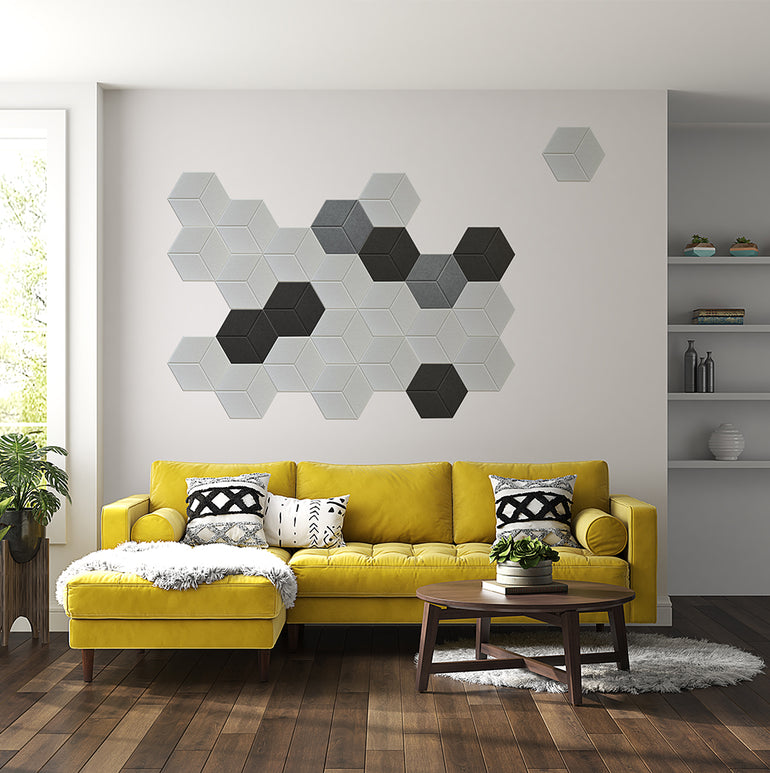Un salon moderne avec un canapé jaune, des coussins à motifs, une table basse ronde en bois et six Panneaux Acoustiques Blanc Texturé by Murs 3D by Wall Decor hexagonaux sur le mur blanc. Le sol en bois et les étagères décoratives complètent l'espace.