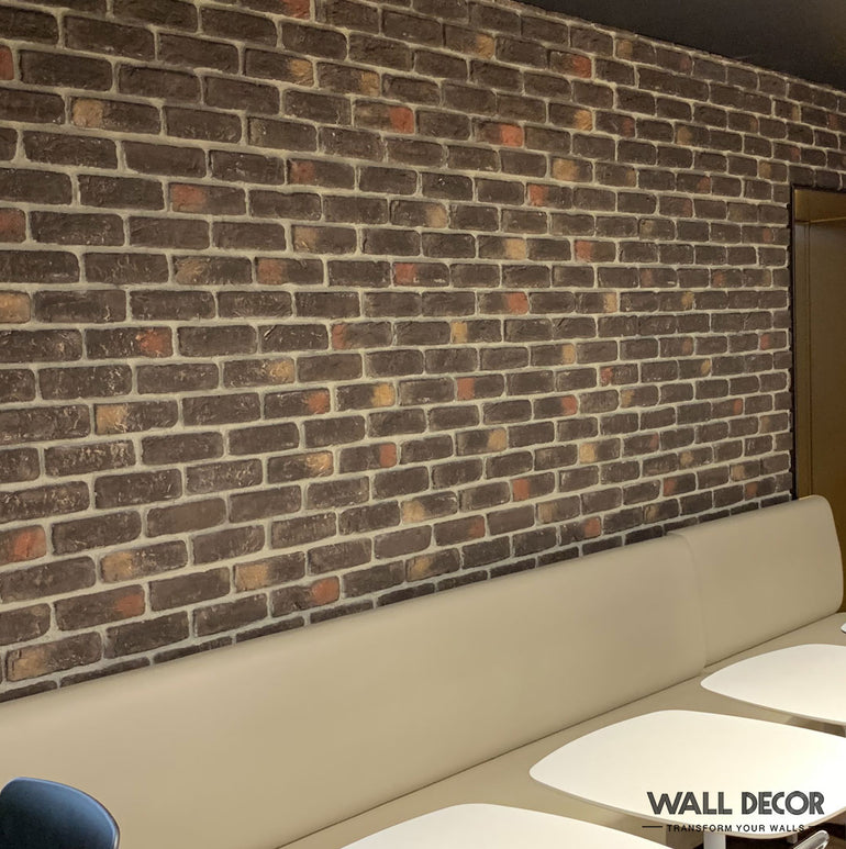 Un coin salon confortable comprend un banc beige coussiné contre un mur rustique Panespol™ Parement Brique vieilli Cassel - Urban Brick, un décor mural élégant et des tables blanches au premier plan. 