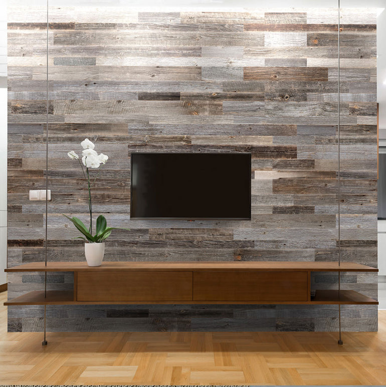 Un salon moderne met en valeur un mur d'accent rustique Parement Bois Anthracite de Wood & Wall Decor™, avec une télévision montée, une étagère flottante en bois et un pot blanc avec une orchidée. Le sol en bois clair renforce l'ambiance chaleureuse.