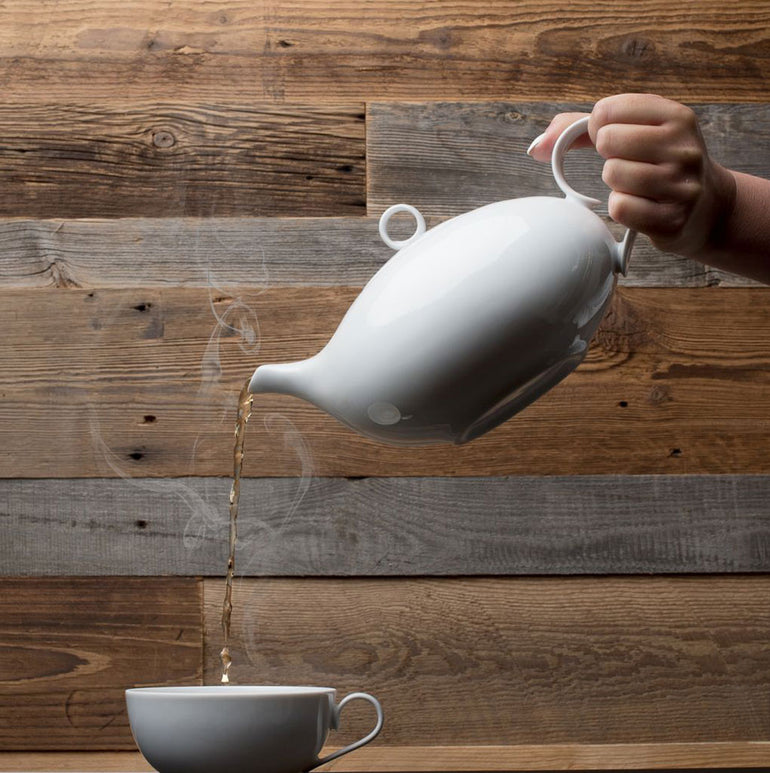 Une main verse du thé fumant dans une tasse sur un fond de panneaux de bois Parement Bois Antik par Wood & Wall Decor™ - laissez-moi vous aider à identifier les mots-clés SEO pour ce cadre serein !.