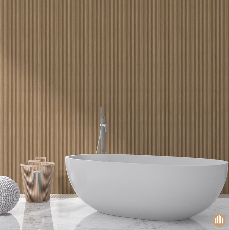 Une salle de bains moderne présente une baignoire ovale blanche sur marbre, un robinet haut et des serviettes dans un panier - évoquant le luxe du spa - placés contre un mur de panneaux de bois Acoupanel™ Panneau Tasseau Hydrofuge effet Chêne Naturel.