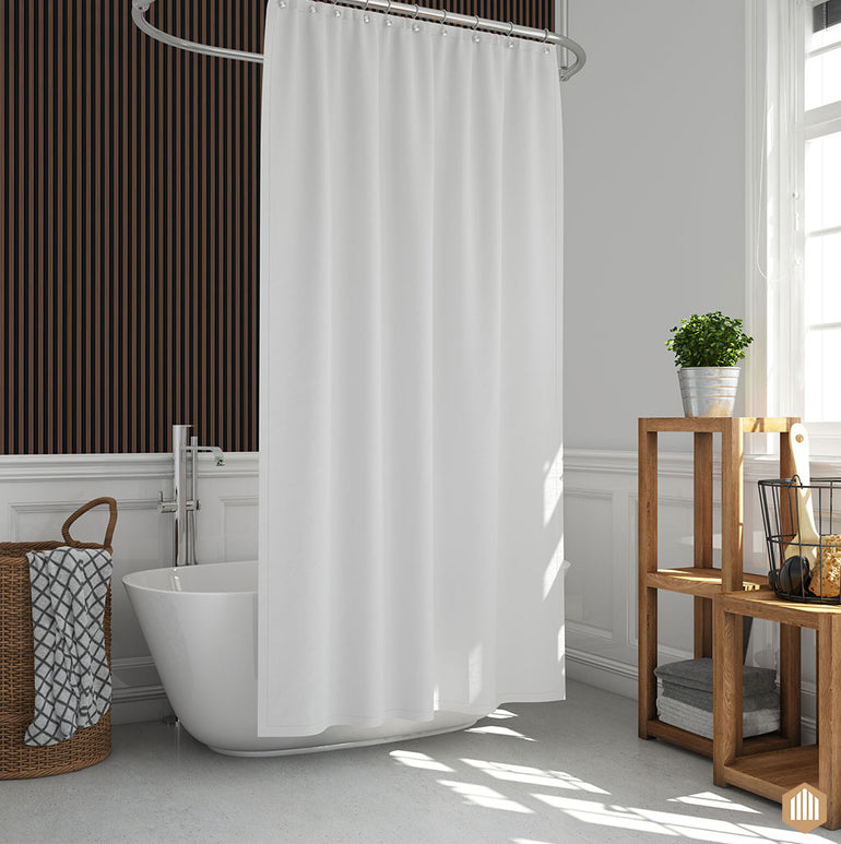 Un rideau de douche gaufré blanc est suspendu à côté d'une baignoire dans une salle de bains moderne avec des murs blancs et un mur d'accent Acoupanel™ Panneau Tasseau Hydrofuge effet Chêne Brun - Fond noir, ainsi qu'un panier à linge et une étagère en bois avec des serviettes, une plante et des articles de toilette.