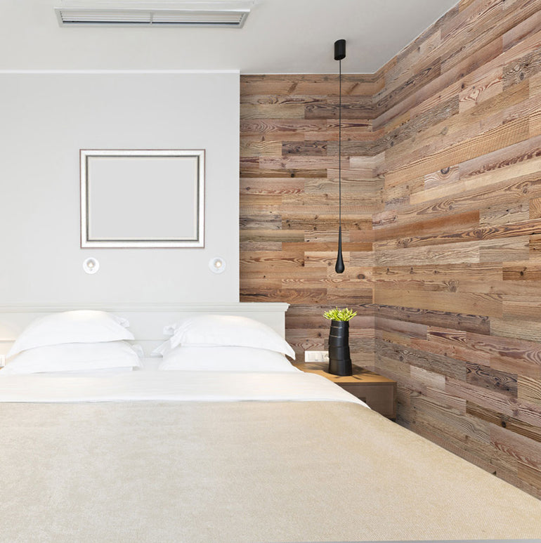 Une chambre à coucher moderne avec un lit et une literie blancs présente un mur d'accent Parement Bois Grange de Wood & Wall Decor™. Une lampe suspendue noire, une petite table de nuit noire et une plante complètent l'atmosphère épurée et apaisante - parfaite pour se détendre.