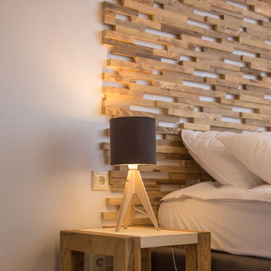 Le Parement Bois Visio de Wood & Wall Decor™ présente une lampe de chevet moderne avec un abat-jour noir sur une table de nuit en bois à côté d'oreillers blancs et d'une tête de lit en bois texturé, mêlant style et fonction pour votre chambre à coucher.