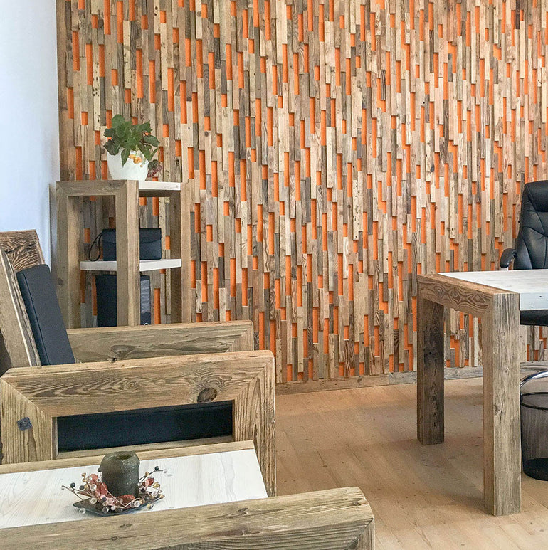 Une pièce moderne avec des meubles en bois rustiques et un mur caractéristique revêtu de panneaux Wood & Wall Decor™ Parement Bois Visio. Des étagères, des tables, des objets de décoration, une plante et une élégante chaise de bureau noire complètent cet espace élégant et fonctionnel.