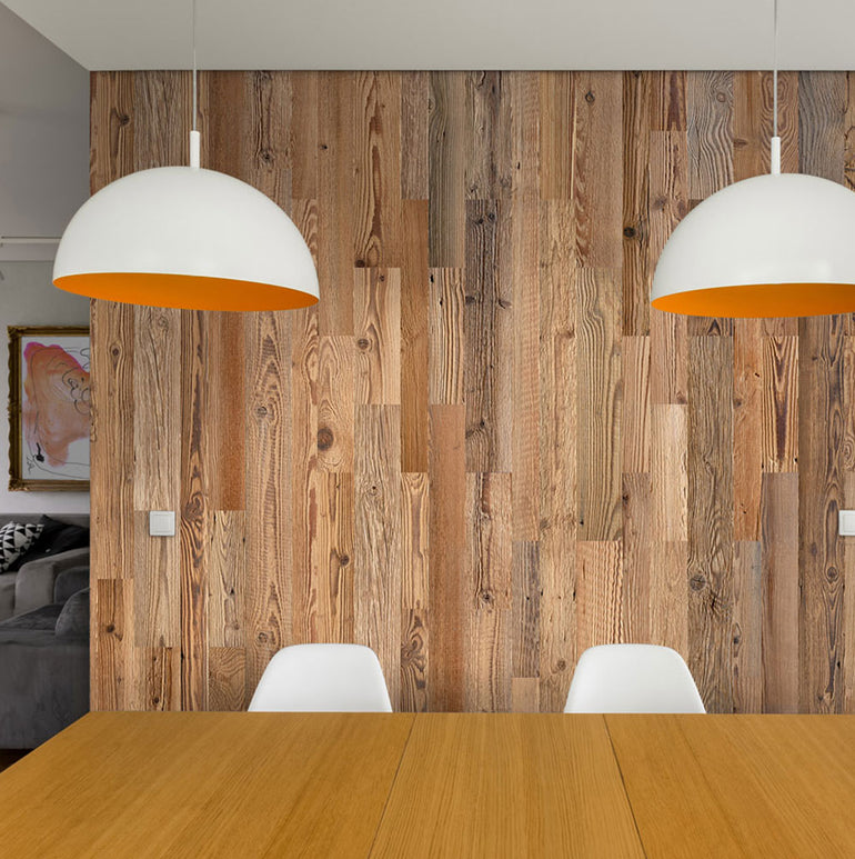 Coin repas moderne avec une table en bois, deux chaises blanches, des lampes suspendues à l'extérieur blanc et à l'intérieur orange, et un mur d'accent en bois Parement Bois Grange par Wood & Wall Decor™.