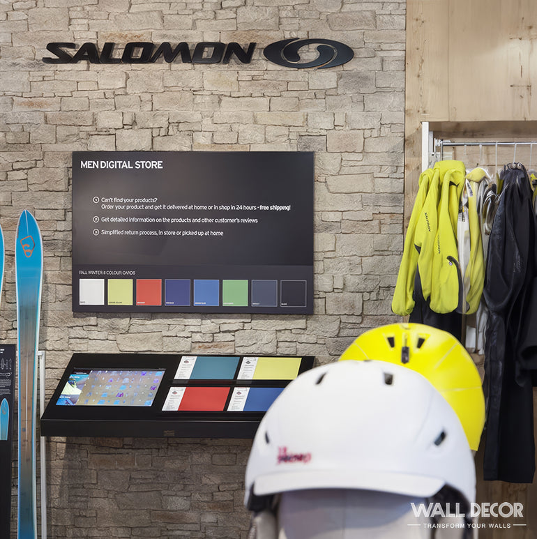 La présentation d'un magasin de détail comprend la marque Panespol™, un écran numérique avec des informations sur les produits, des équipements de ski colorés, des vestes sur cintres et des casques blancs au premier plan sur un fond de mur de briques Parement Pierre Terruel foncé.