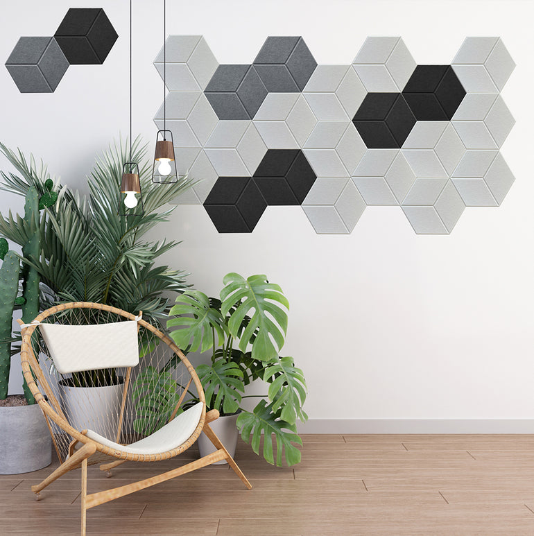 Une pièce moderne avec une chaise en rotin, des plantes vertes et des lampes suspendues. Le mur blanc affiche Murs 3D de Wall Decor Panneaux Acoustiques Blanc Texturé - six panneaux adhésifs hexagonaux dans un agencement géométrique saisissant.