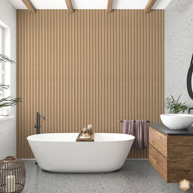 Une salle de bains moderne avec une baignoire blanche autoportante, un plateau en bois, une serviette drapée sur le côté et des lattes Acoupanel™ Panneau Tasseau Hydrofuge effet Chêne Naturel sur le mur. Des armoires en bois, un lavabo et des plantes complètent le tout.