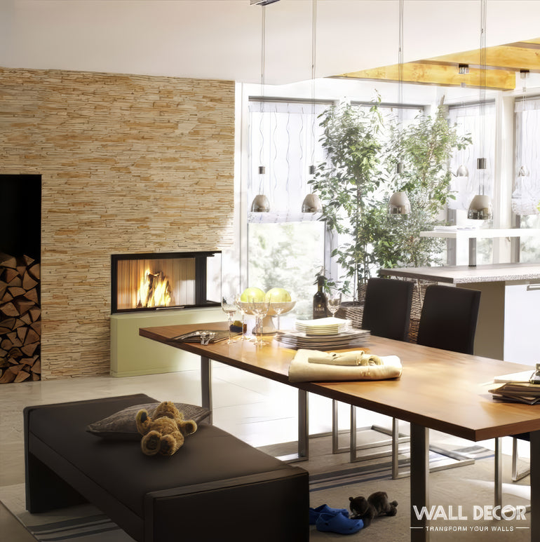 Une salle à manger moderne présente une table en bois, un banc avec un ours en peluche et un jouet, et une cheminée en pierre Panespol™ Parement Pierre beige - Laja Fina. De grandes fenêtres donnent sur une verdure luxuriante et du bois de chauffage empilé complète la scène douillette.