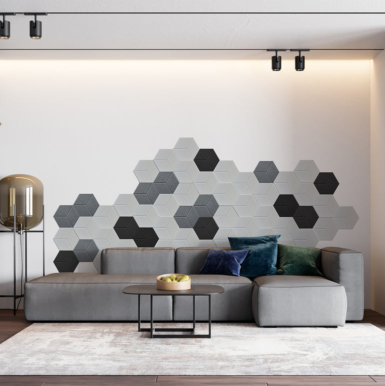 Ce salon moderne est composé d'un canapé gris, de coussins colorés et d'une table basse ronde. Le point fort est un mur acoustique avec des carreaux hexagonaux Murs 3D by Wall Decor Panneaux Acoustiques Blanc Texturé. Une lampe haute se trouve à gauche.