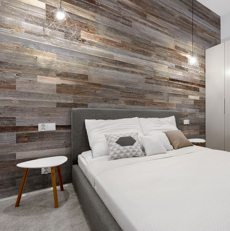 Chambre à coucher moderne avec un lit capitonné gris, une literie blanche, des oreillers géométriques, un mur d'accent Wood & Wall Decor™ Parement Bois Anthracite, deux lampes suspendues, une table d'appoint ronde blanche avec des pieds en bois, et une armoire de couleur claire.